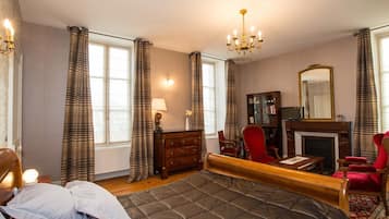 Een slaapkamer met een groot bed, een bureau, een stoel, een open haard en een spiegel.