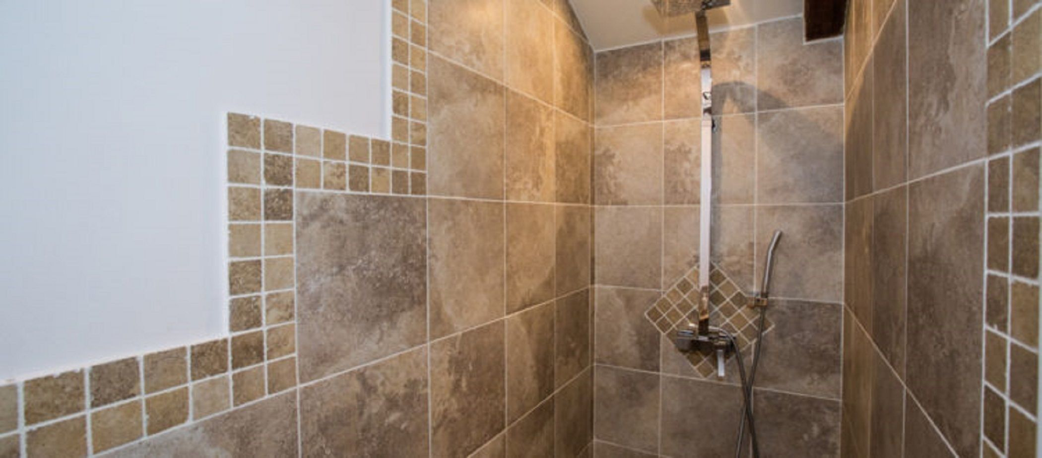 A shower area with beige tiles and a handheld showerhead.