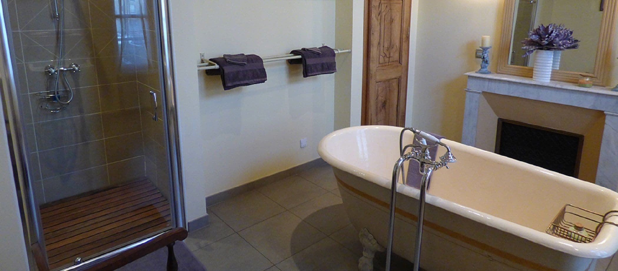 Ein Badezimmer mit einer gläsernen Dusche, einer freistehenden Badewanne und einer hölzernen Sitzbank.