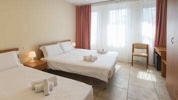 A hotel room with two beds, a desk, a chair, and a window with curtains.