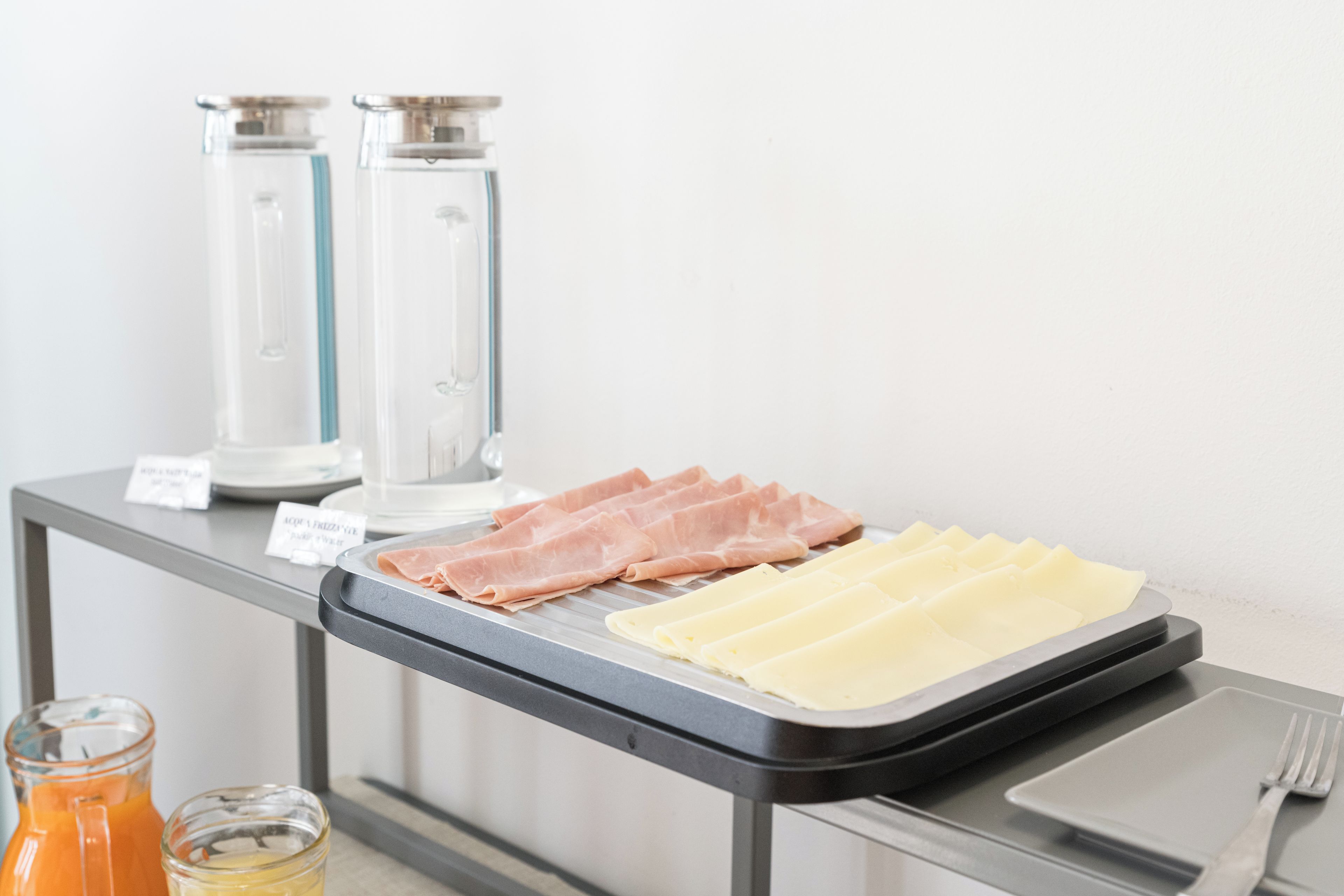A buffet table with sliced meats and cheese, a juice pitcher, and a water dispenser.