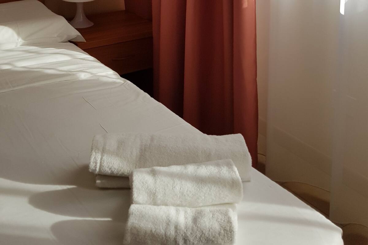 Une chambre d’hôtel avec un lit bien fait, une lampe de chevet et une fenêtre avec des rideaux.