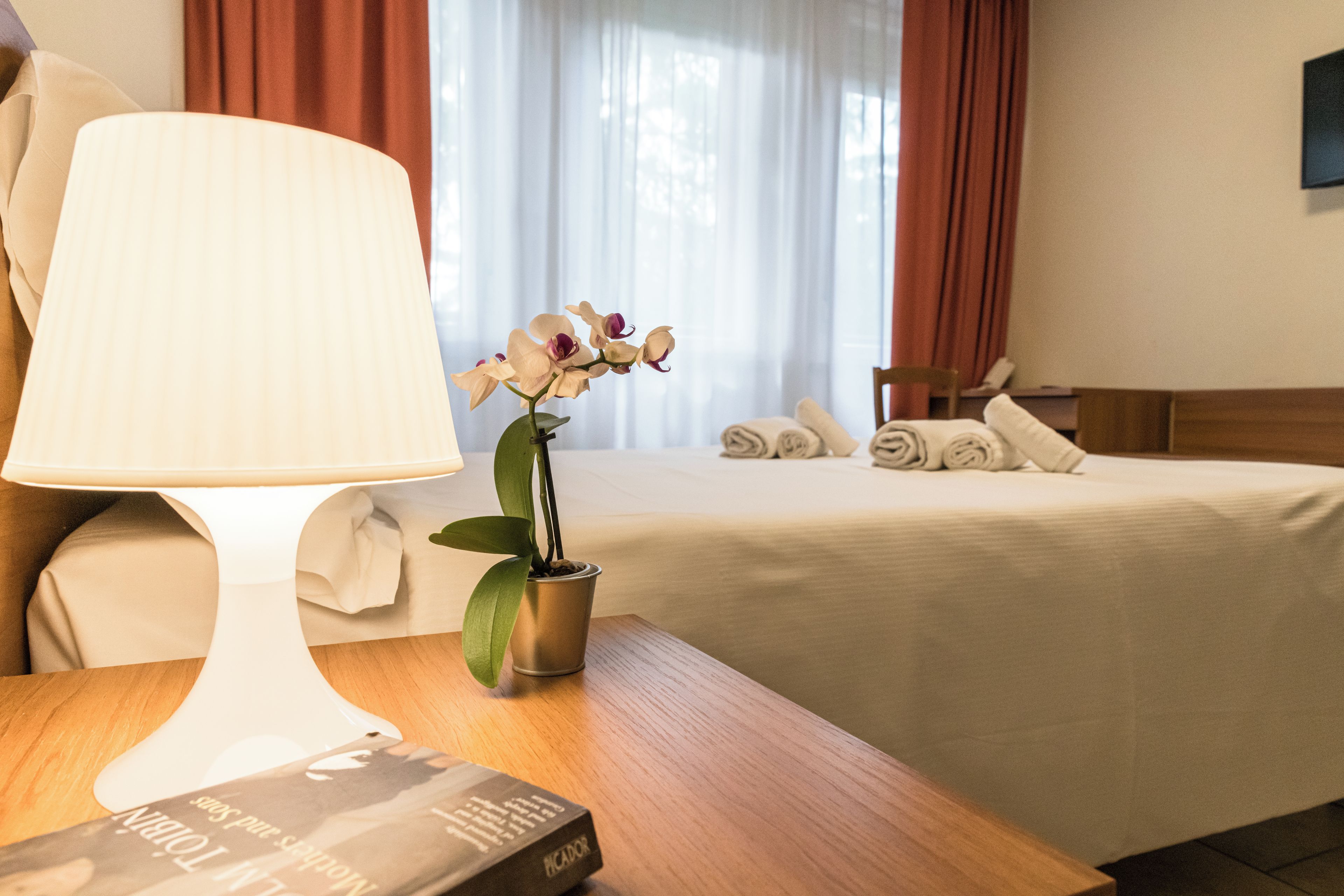 A hotel room with a bed, a bedside table with a lamp, a potted orchid, and neatly folded towels.