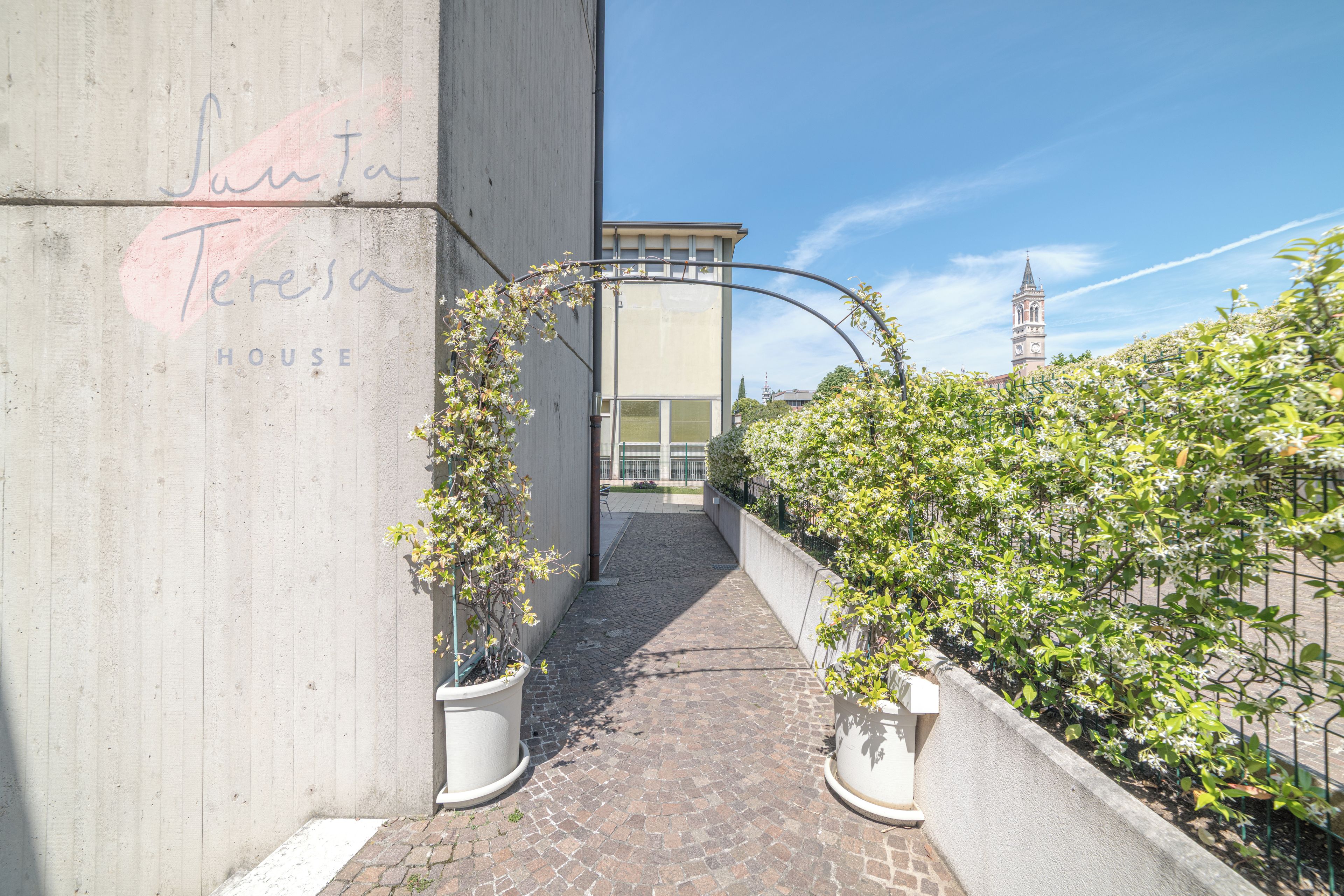 Un estrecho callejón con un muro de concreto a la izquierda y una valla metálica a la derecha, que conduce a la entrada de un edificio.