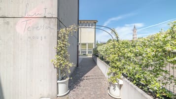 Un estrecho callejón con un muro de concreto a la izquierda y una valla metálica a la derecha, que conduce a la entrada de un edificio.