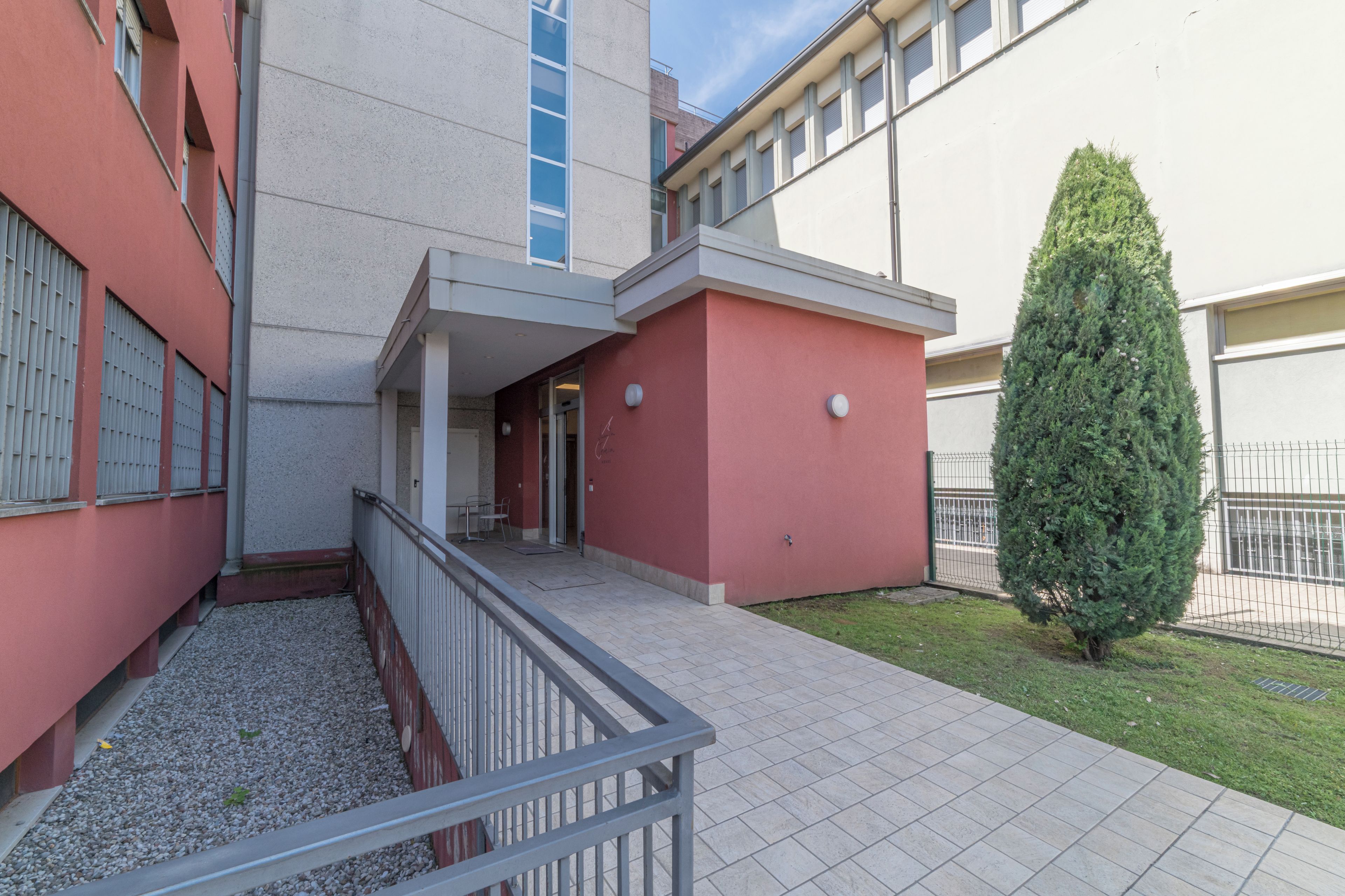 Un edificio con fachada roja, un pequeño patio con un árbol y una entrada con reja.