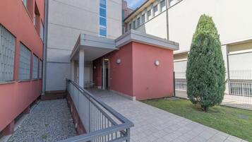 Un edificio con fachada roja, un pequeño patio con un árbol y una entrada con reja.