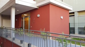 A building with a red facade, a glass entrance, and a metal railing in the foreground. - Santa Teresa House (Verona)