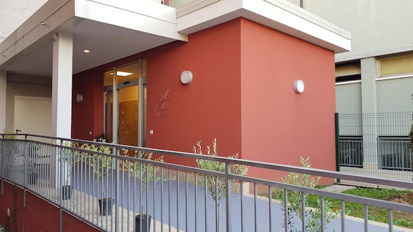 A building with a red facade, a glass entrance, and a metal railing in the foreground. - Santa Teresa House (Verona)
