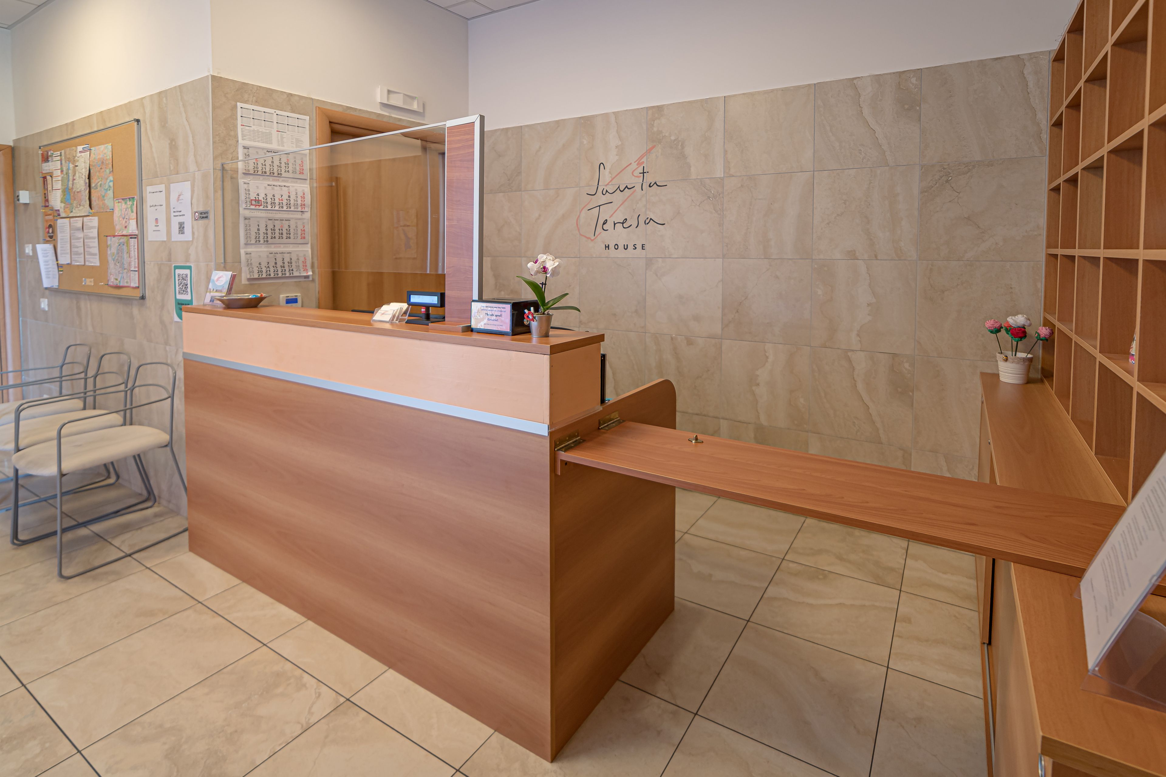 Un mostrador de recepción con detalles de madera, un calendario, una computadora y una orquídea en maceta.