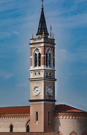 A clock tower with a pointed spire, two visible clock faces, and the inscription "PUIUT HORO" on the tower. - Santa Teresa House (Verona)
