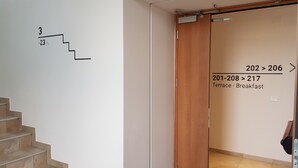 Interior d'hotel amb una escala numerada, una porta corredissa amb indicació de números de habitació i un senyal que mostra una terrassa i zona de l'esmorzar.
