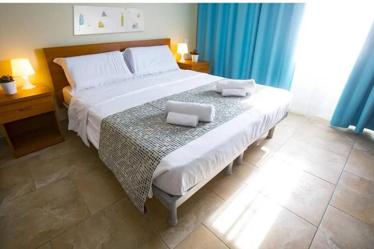 Un lit bien fait, avec des draps blancs, un plaid à motifs et deux serviettes.