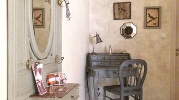 A room with a vintage-style dresser, a mirror, a hat on the wall, a desk with a lamp, and a chair.