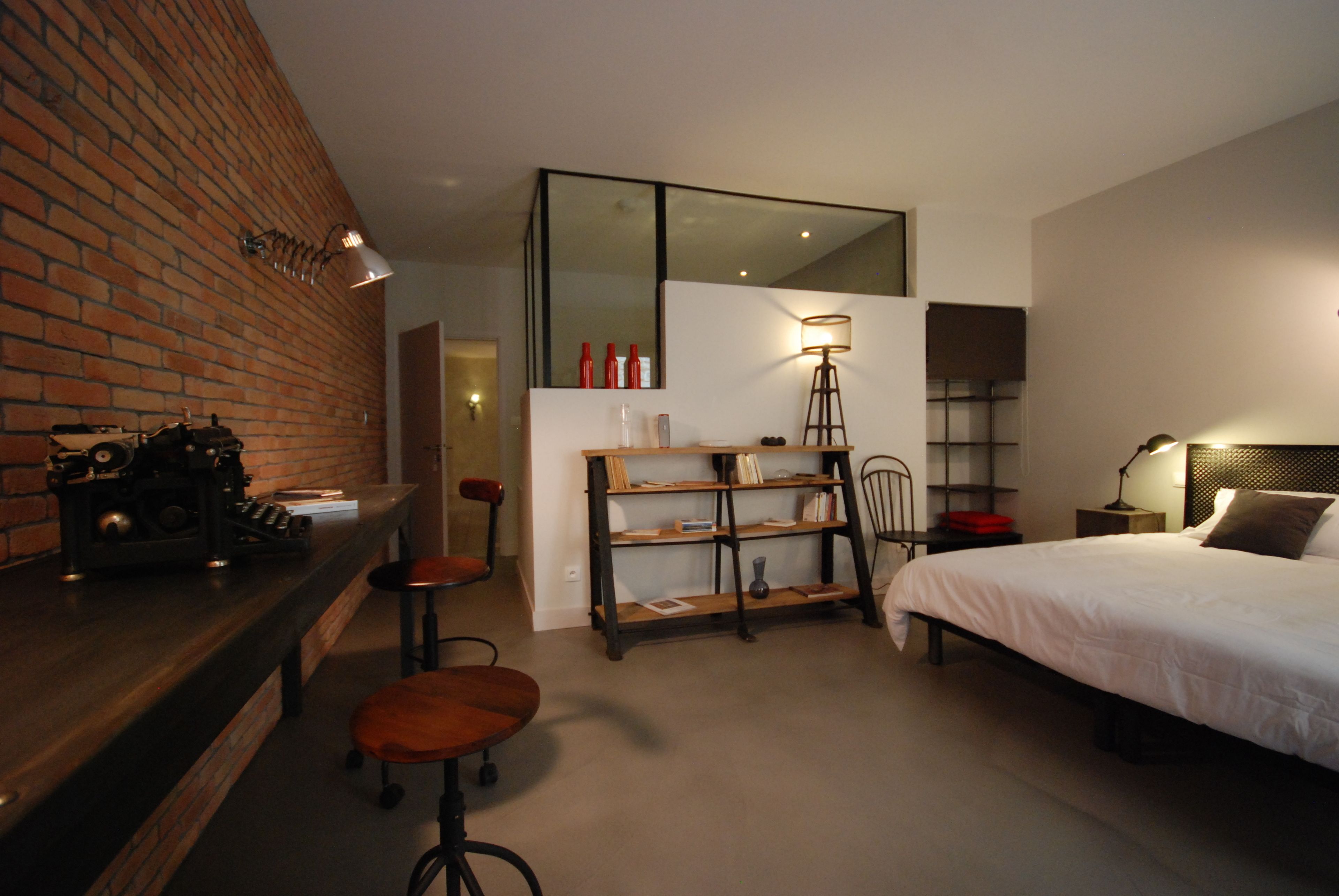 Une chambre moderne avec un grand lit, un bureau avec une chaise, une bibliothèque et un mur en briques.