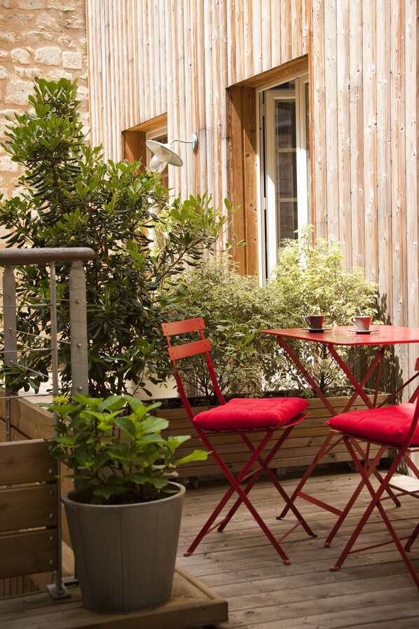 An outdoor patio with a wooden table and red chairs, surrounded by potted plants and a stone wall. - L'Esprit des Chartrons (Bordeaux)