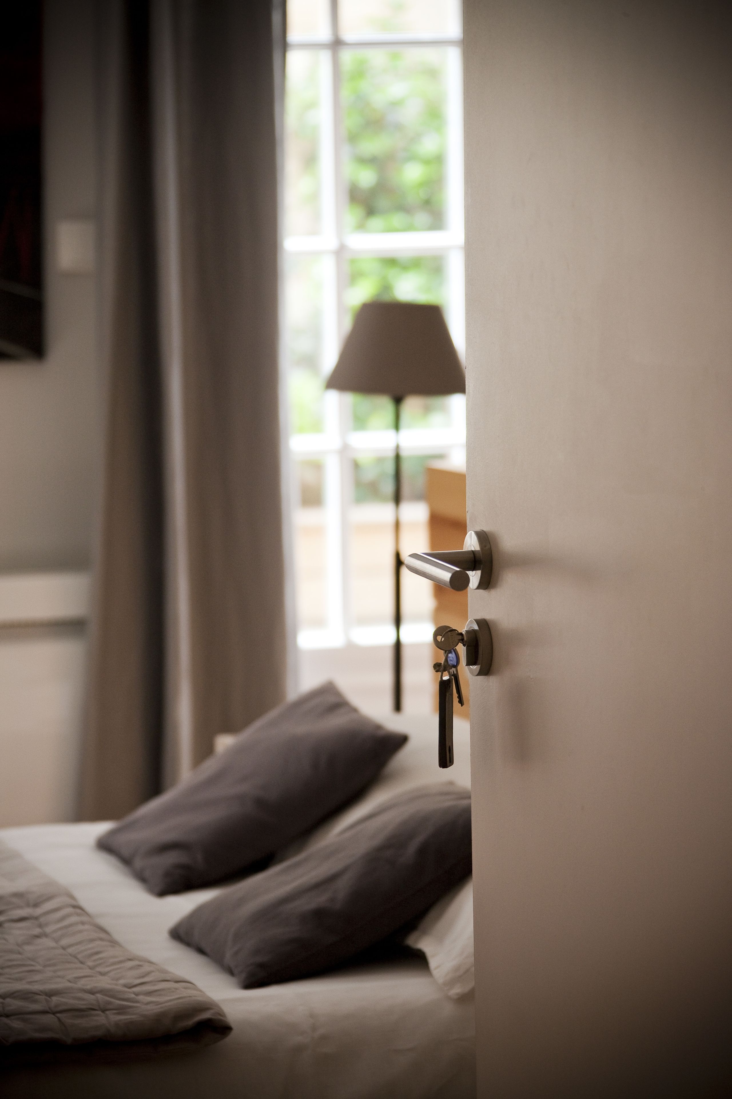 A hotel room with a bed, pillows, a door with a key in the lock, and a window with curtains.