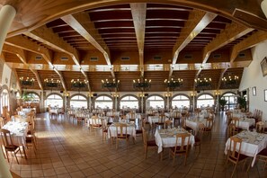 A spacious dining hall with high wooden ceilings and multiple tables set for dining.