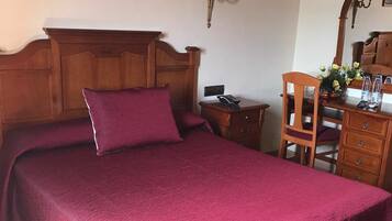 A bedroom with a wooden headboard, a large bed with a red bedspread, a nightstand, a wooden dresser, and a mirror.