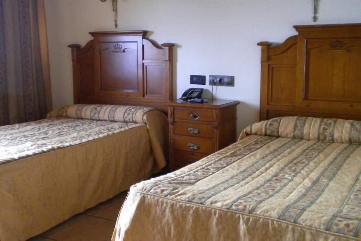 A hotel room with two single beds, a wooden dresser, a telephone, and a wall socket.