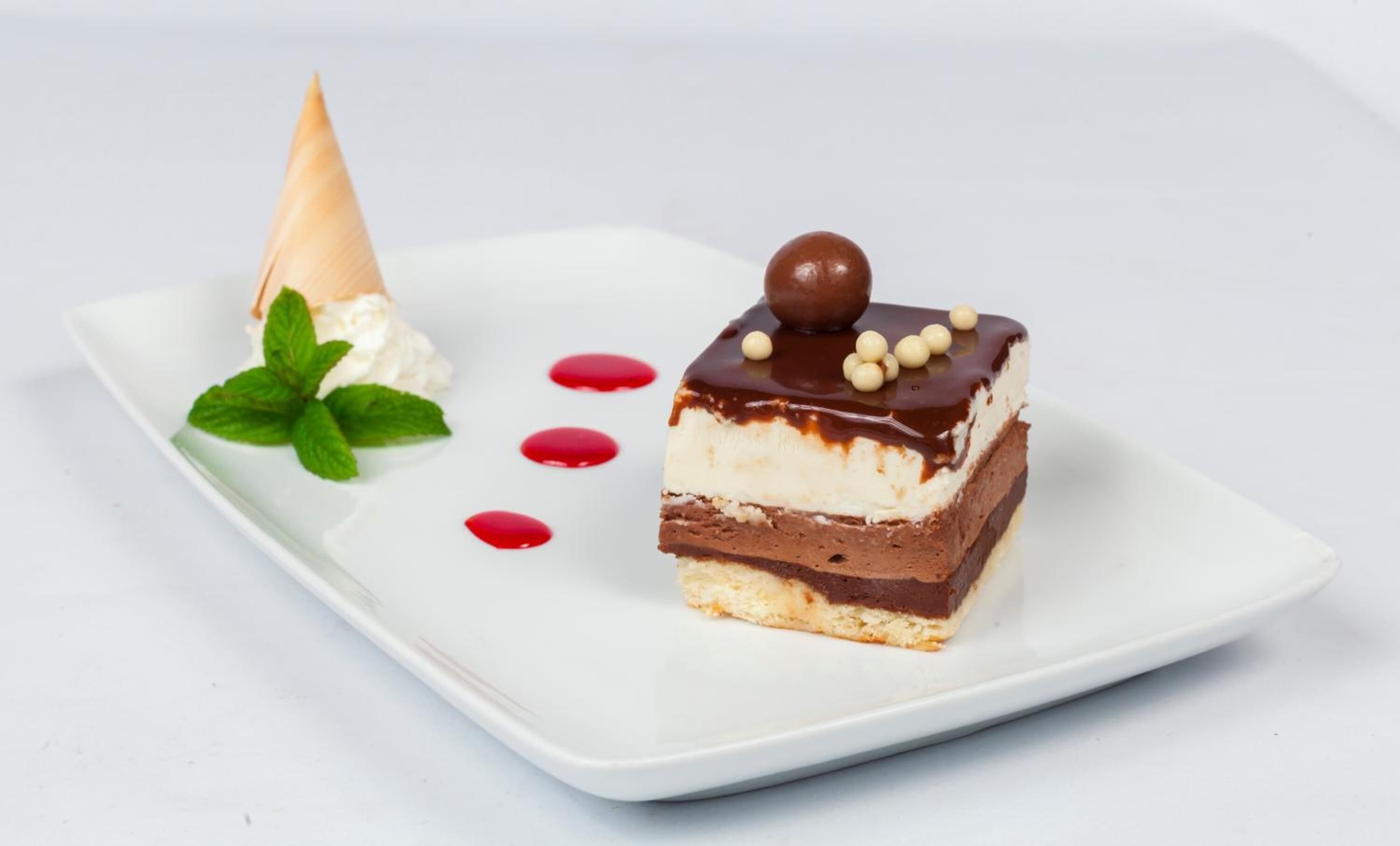 A dessert on a white plate with mint leaves and red sauce.
