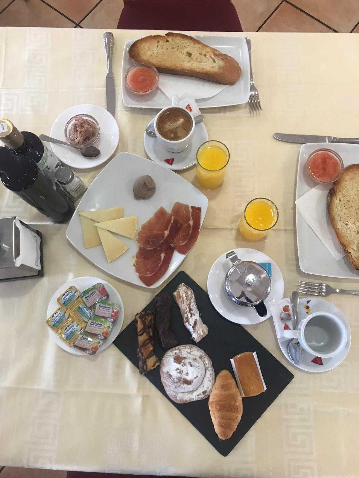 Een ontbijttafel met diverse soorten eten, zoals brood, kaas, vleeswaren en drankjes.
