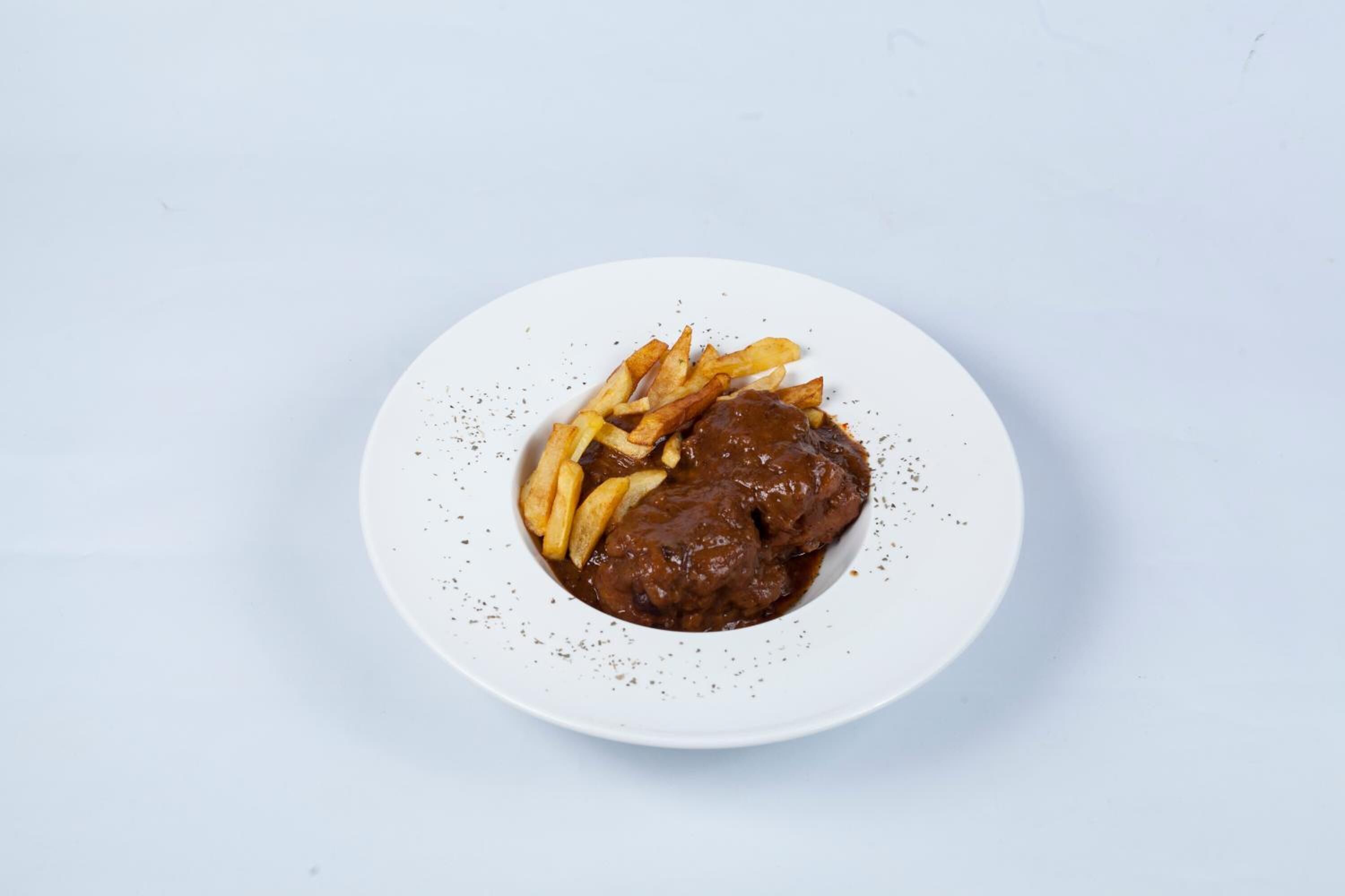 A plate with a meat dish and fries on a white plate.