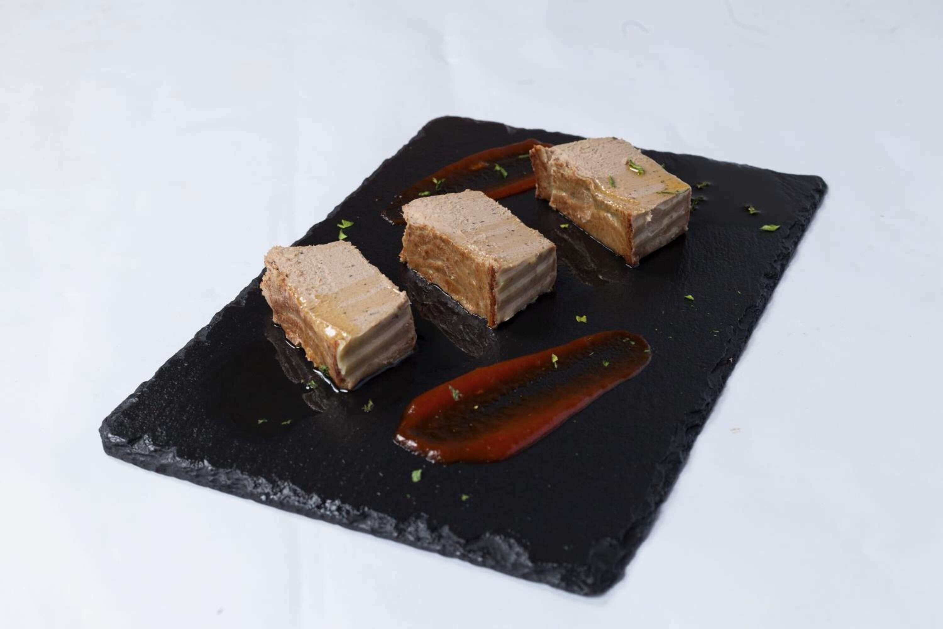 Un postre sobre un plato de pizarra negra, con salsa roja y decoración.