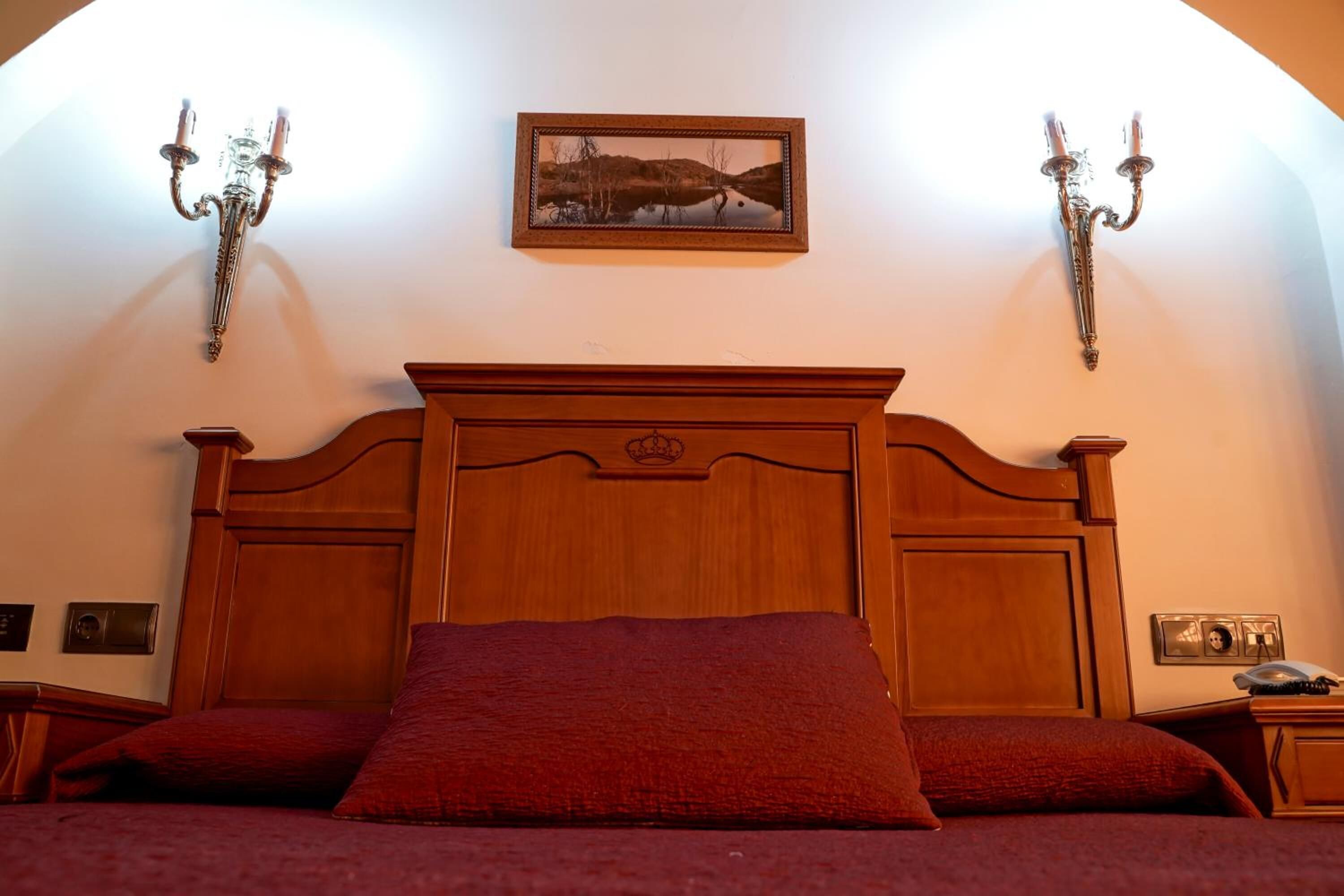 Une chambre à coucher avec un lit en bois, une literie rouge, un tableau encadré au mur et des appliques murales.