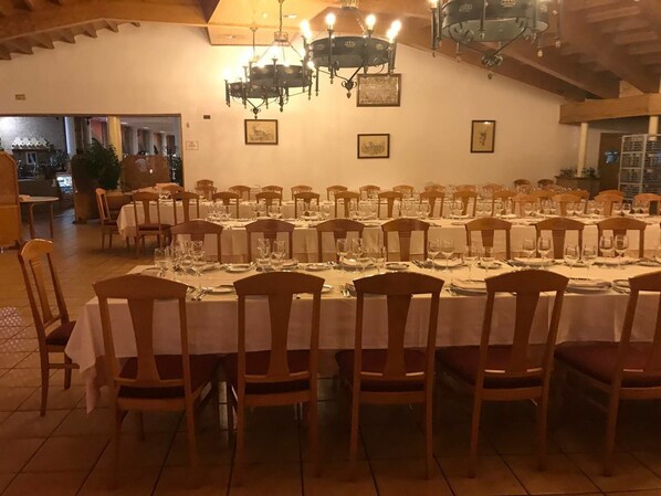 A dining area with long tables set for a meal, wooden chairs, and chandeliers.