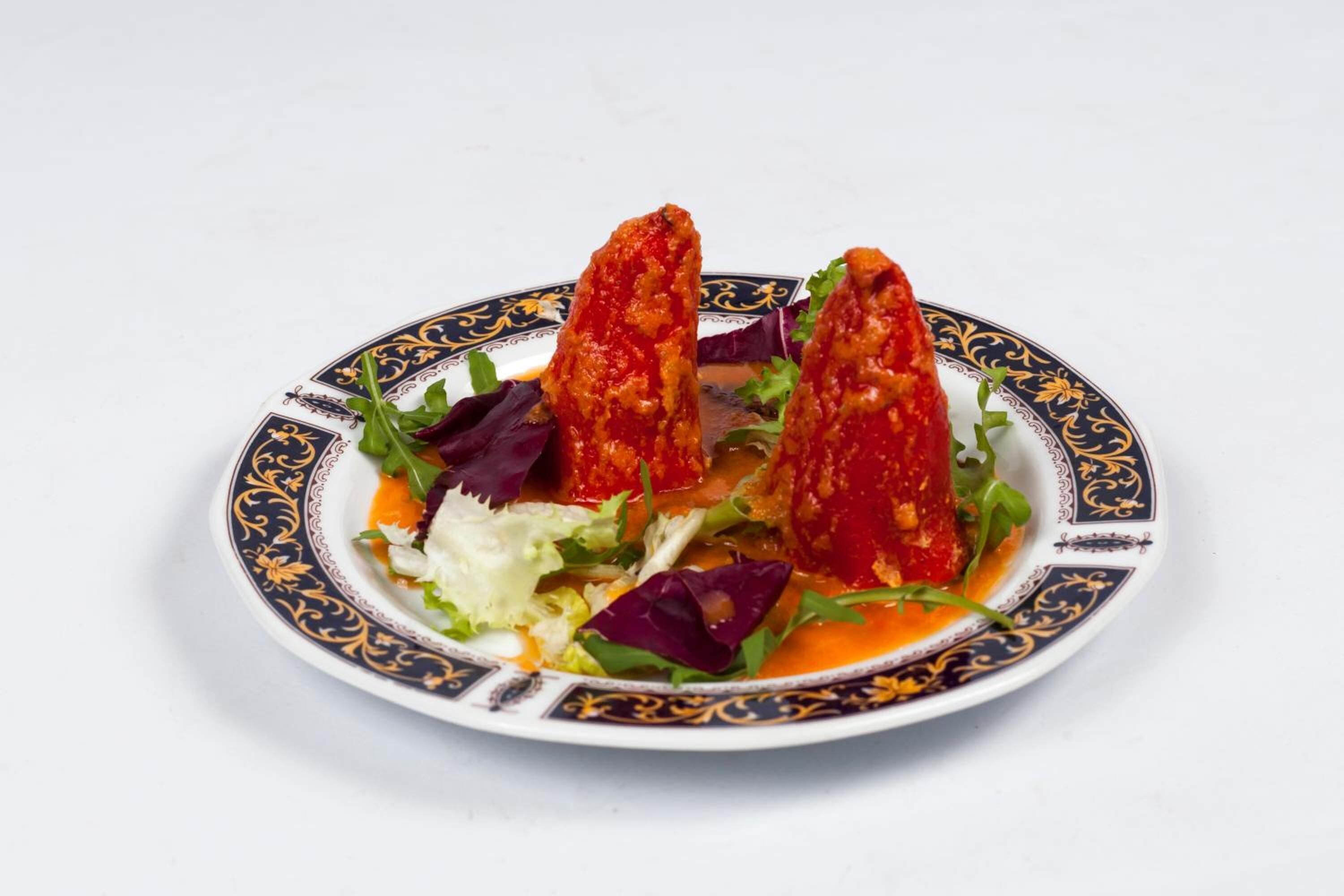 Une assiette ornée d’un bord décoratif, contenant une salade composée de différentes variétés de légumes verts et d’une sauce rouge.
