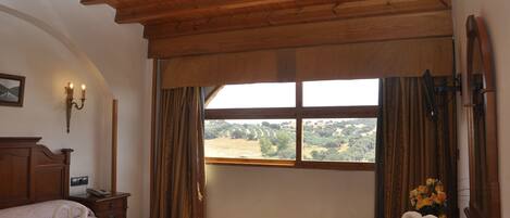 A hotel room with a wooden ceiling, a large window with curtains, a bed with a towel arrangement, and a nightstand with a lamp.