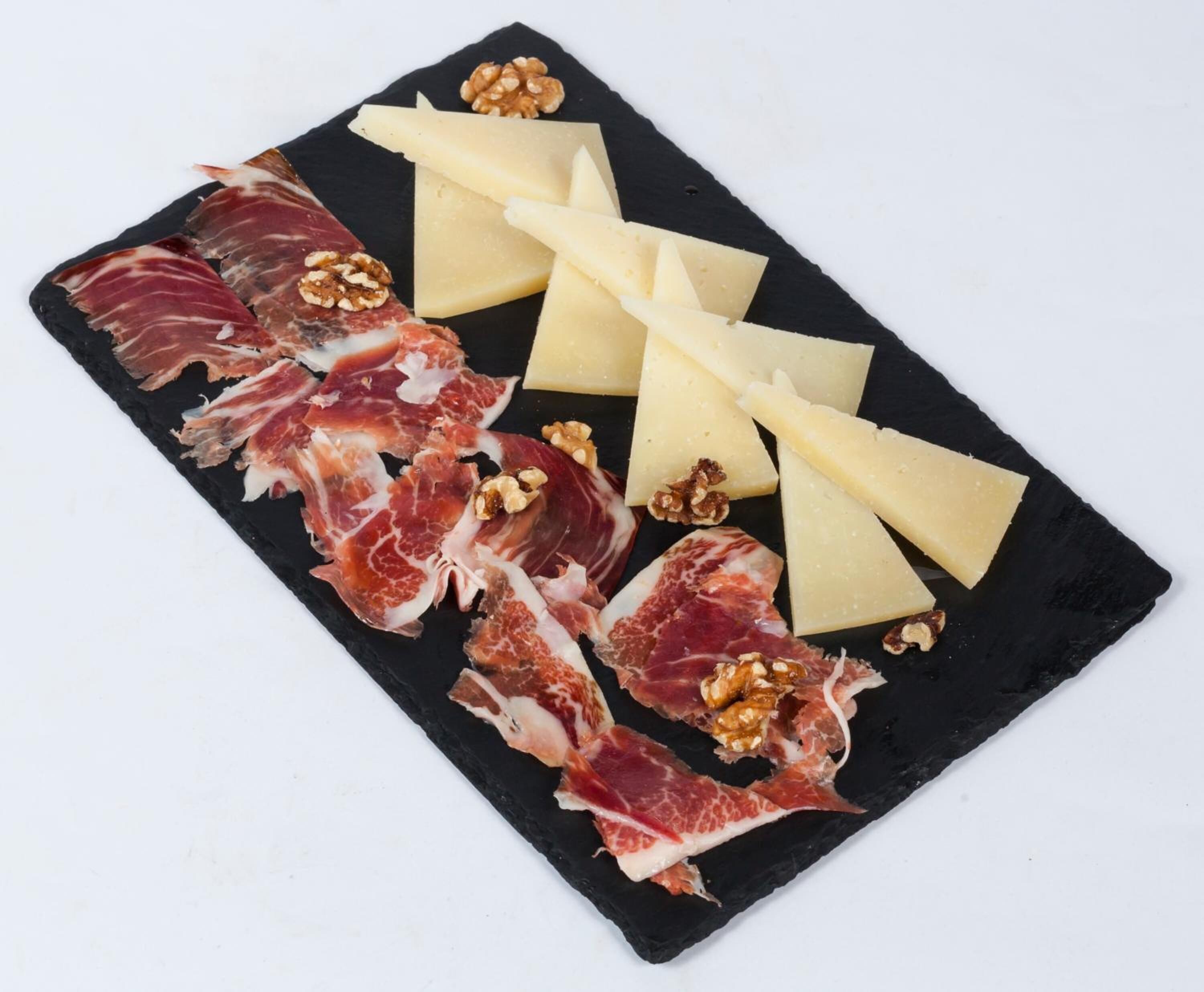 Eine schwarze Schiefertafel mit luftgetrocknetem Schinken, Käse und Walnüssen.