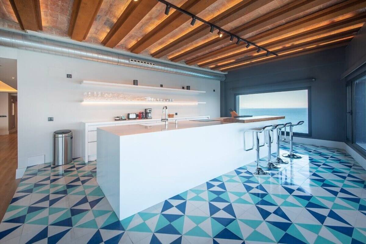 Uma cozinha moderna com ilha central, eletrodomésticos de aço inoxidável e piso com padrão geométrico.