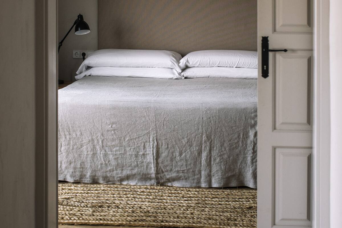 Quarto com cama, luminária de cabeceira e tapete de fibras no chão.