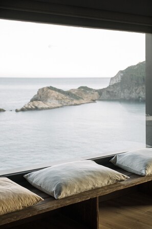 A wooden bench with pillows by a window overlooking a coastal view. - Apartaments Cap Sa Sal (Begur)