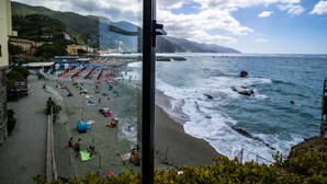A beach with umbrellas and people, a rocky shoreline, and mountains in the background. - La Casa del Gigante Luxury Collection (Monterosso al Mare)