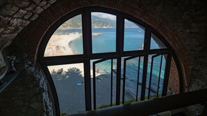 A view through a large arched window overlooking a beach with clear blue water and a distant mountain range. - La Casa del Gigante Luxury Collection (Monterosso al Mare)
