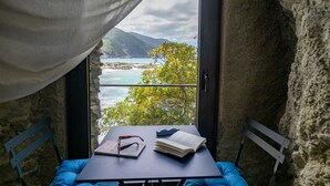 A table with a book and glasses, two blue cushioned chairs, and a view of a coastal landscape through a window. - La Casa del Gigante Luxury Collection (Monterosso al Mare)