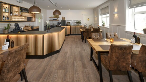 A modern restaurant with a curved wooden bar, dark upholstered chairs, and a wooden floor. - Hjørring Kro (Hjørring)