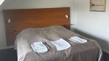A single bed with a wooden headboard, a gray bedspread, and neatly folded white towels on the bed.