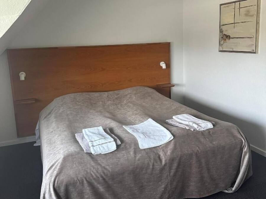 A single bed with a wooden headboard, a gray bedspread, and neatly folded white towels on the bed.