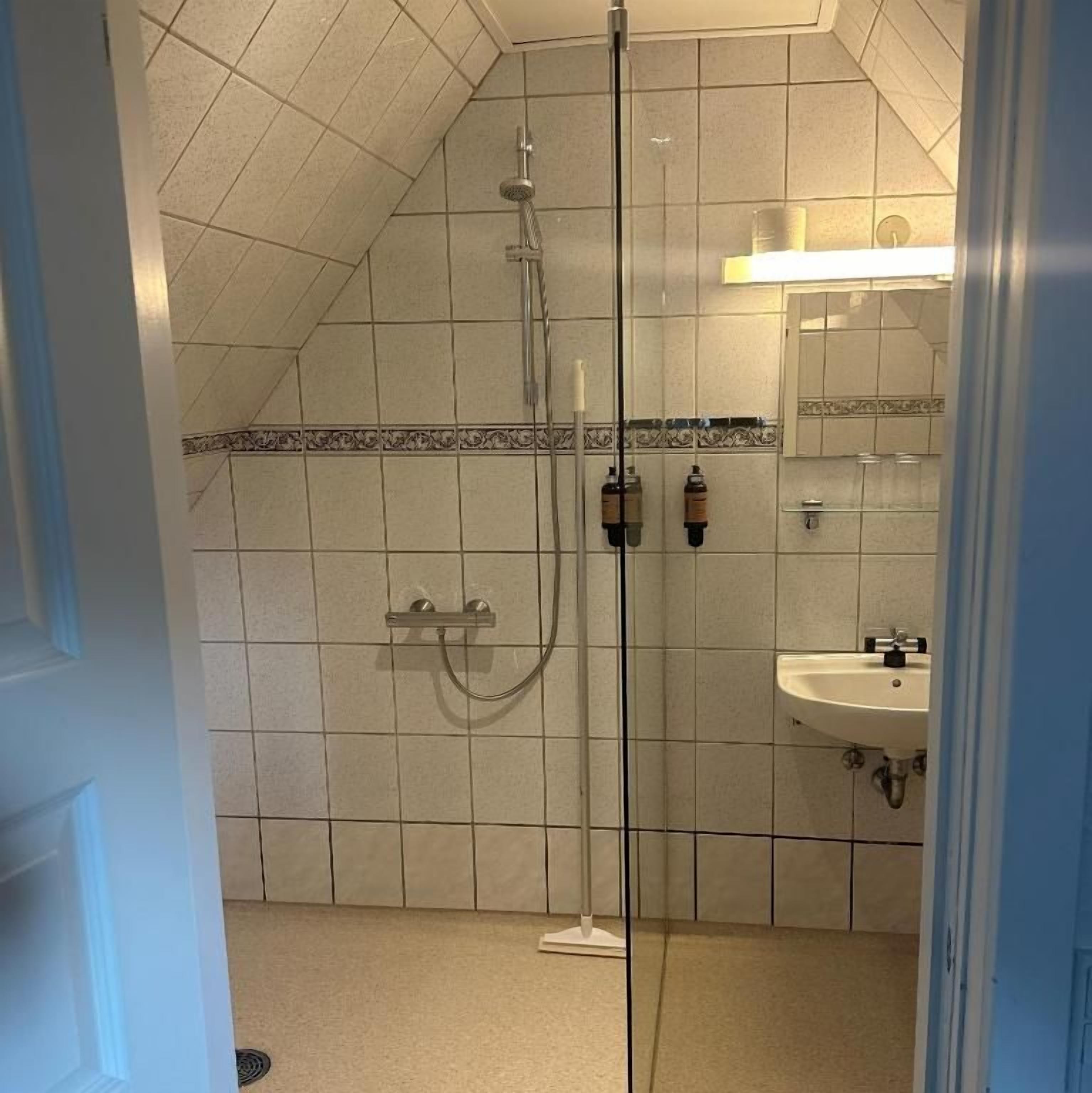 Et badeværelse med en glasafskærmet brusekabine, et håndvask og klinkegulv.