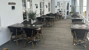 A covered outdoor patio with multiple tables and wicker chairs, white walls, and a wooden deck. - Hjørring Kro (Hjørring)
