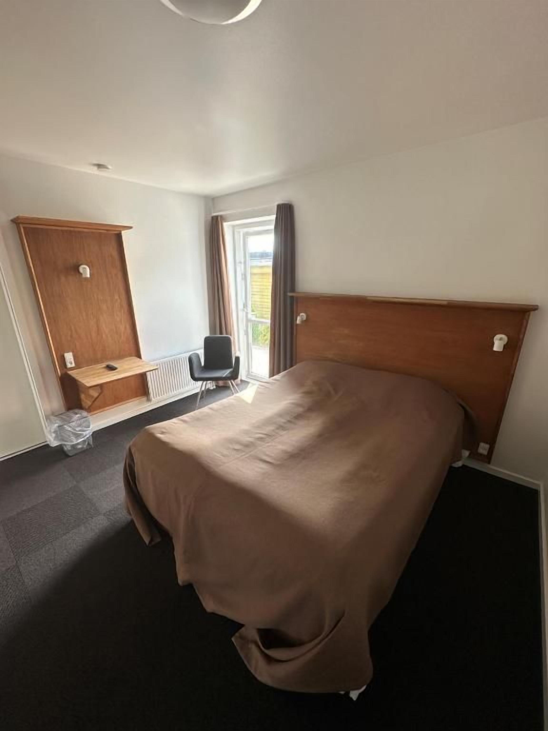 Habitación de hotel con una cama individual, cabecera de madera, escritorio con silla y ventana con cortinas.