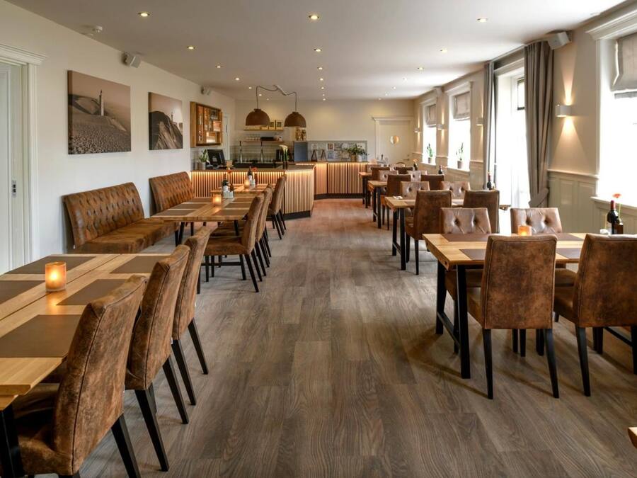 A spacious dining area with multiple tables and chairs, a kitchen in the background, and artwork on the walls.