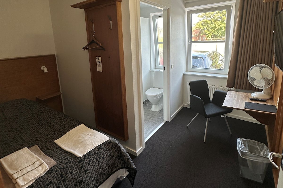 Hotellihuone, jossa on sänky, työpöytä, tuoli, ikkuna ja ovi.
