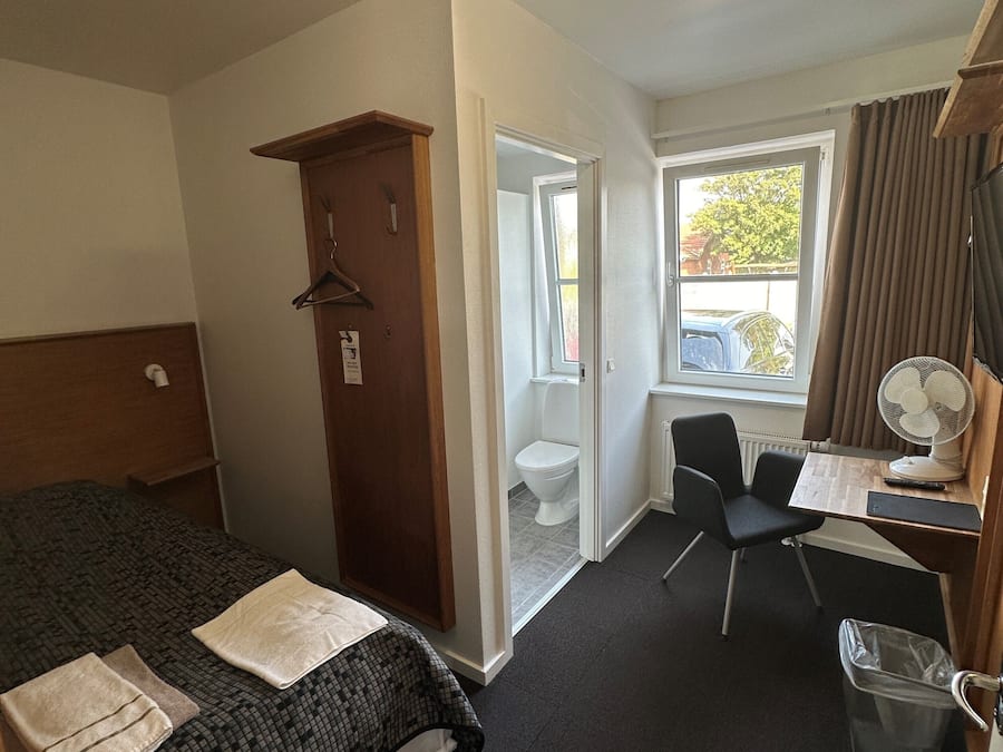 Habitación de hotel con una cama, un escritorio, una silla, una ventana y una puerta.