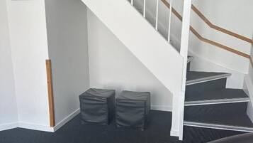 A staircase with white railings and a black carpeted floor. There are two black cushioned stools and a black leather sofa with a red cushion.
