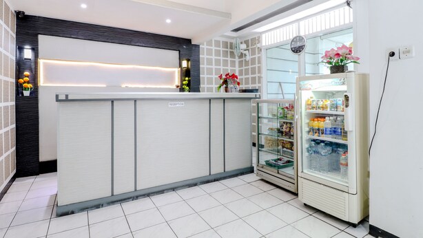 Un área de recepción con mostrador, un refrigerador lleno de bebidas y un reloj en la pared.